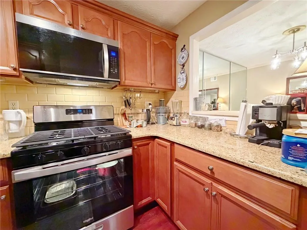 Kitchen featuring stainless steel appliances, light stone countertops, backsplash, and decorative light fixtures