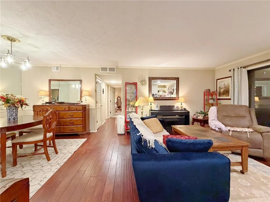 Living area featuring crown molding, wood-type flooring, suspended lighting, and a textured ceiling