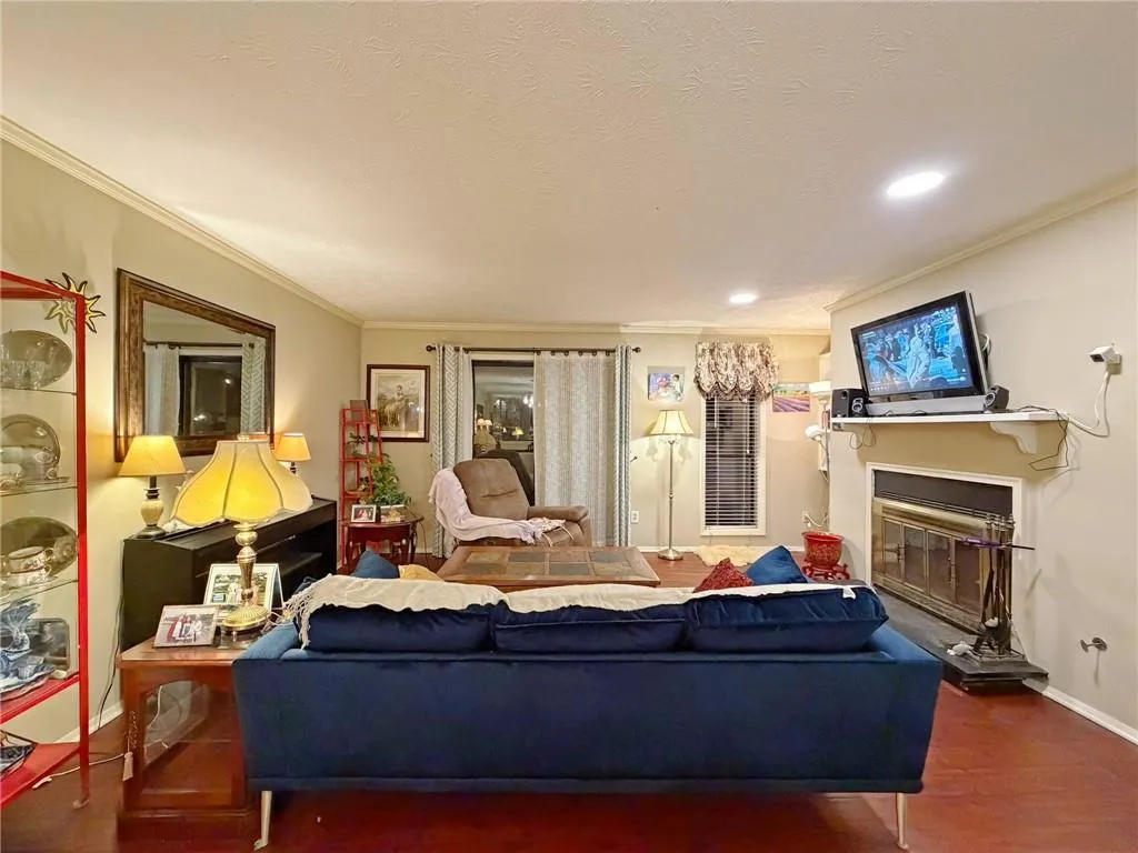 Living room with wood finished floors, crown molding, a glass covered fireplace, and recessed lighting