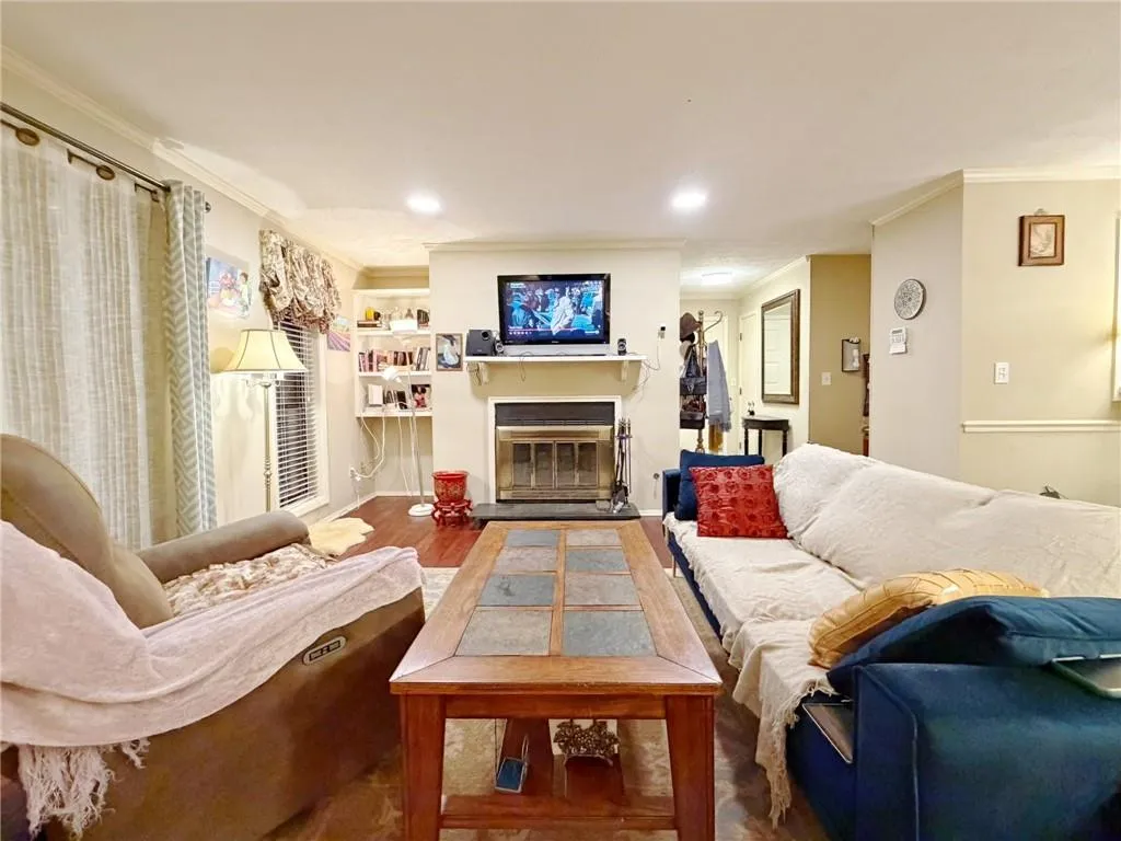 Living area with crown molding, a glass covered fireplace, wood finished floors, and recessed lighting