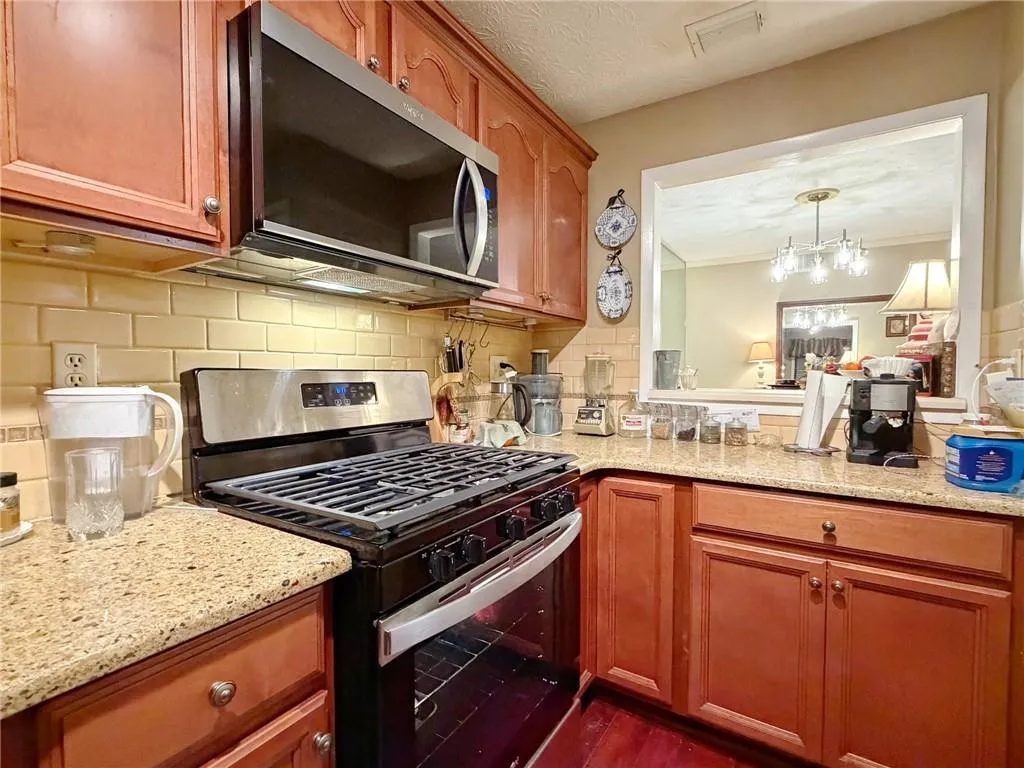 Kitchen with stainless steel appliances, decorative backsplash, light stone countertops, wood finish cabinets, and ornamental molding