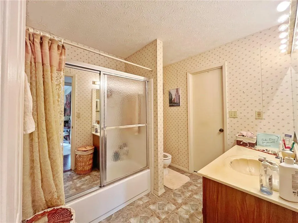 Full bathroom featuring a textured ceiling, combined bath / shower with glass door, and vanity