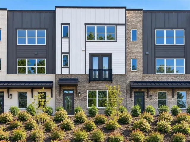 Modern townhome exterior featuring a combination of light brick, dark paneling, and white siding