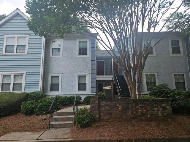 Stucco and siding exterior with multiple windows, concrete walkway, and brick-finished planter