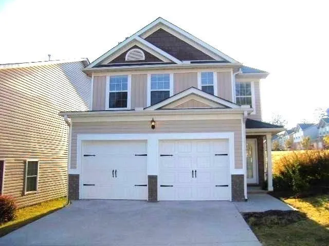 Two-story exterior with light-colored siding, a two-car garage, stone accents, a covered front entry, and a concrete driveway