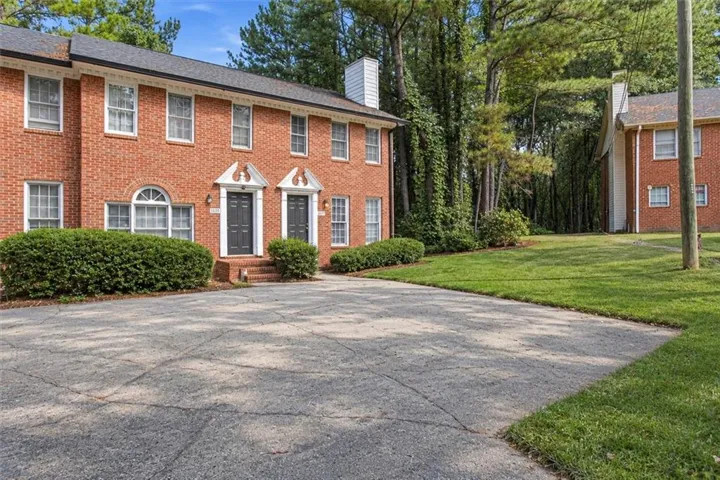 Brick exterior with white window trim, dual entry doors with decorative pediments, and a paved parking area