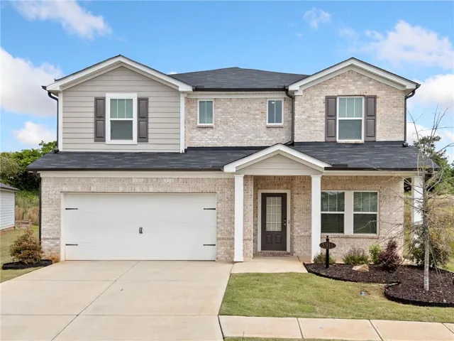 Two-story exterior with light brick and siding, featuring a two-car garage, covered entry, and landscaped front yard