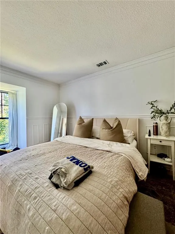 Bedroom with a textured ceiling, ornamental molding, a wainscoted wall, and a decorative wall
