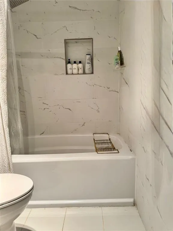Bathroom featuring shower / bath combo with shower curtain, tile patterned flooring, and tile walls