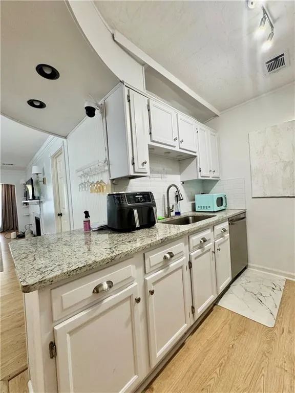 Kitchen featuring backsplash, light wood-style flooring, light stone counters, white microwave, and white cabinets