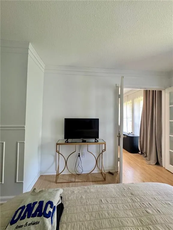 Bedroom featuring ornamental molding, light wood-style flooring, and a textured ceiling