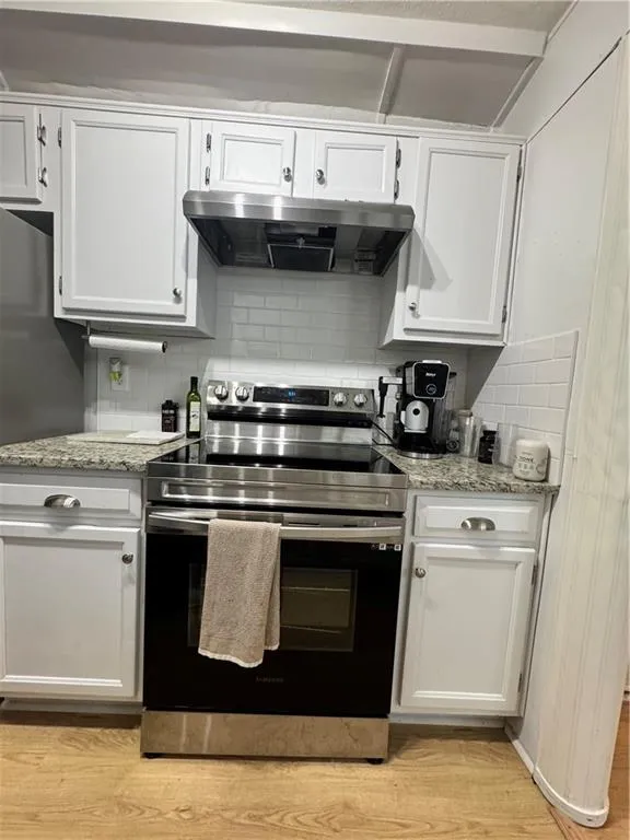 Kitchen featuring stainless steel electric range oven, backsplash, white cabinets, and exhaust hood