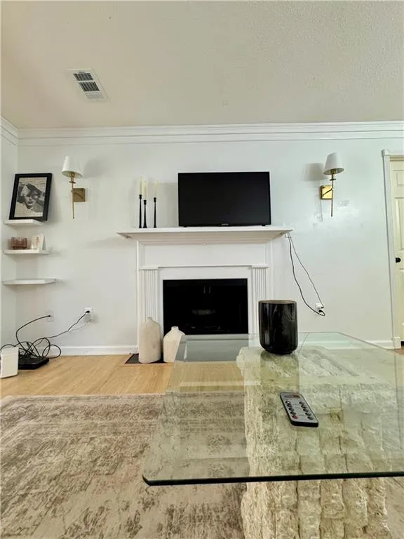 Living room featuring crown molding, a fireplace with flush hearth, and wood finished floors