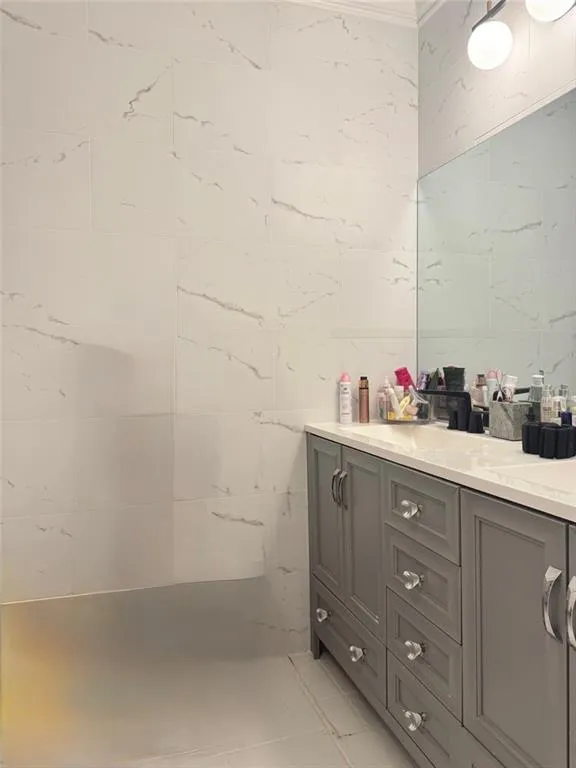 Bathroom with vanity, light tile patterned floors, crown molding, and tile walls
