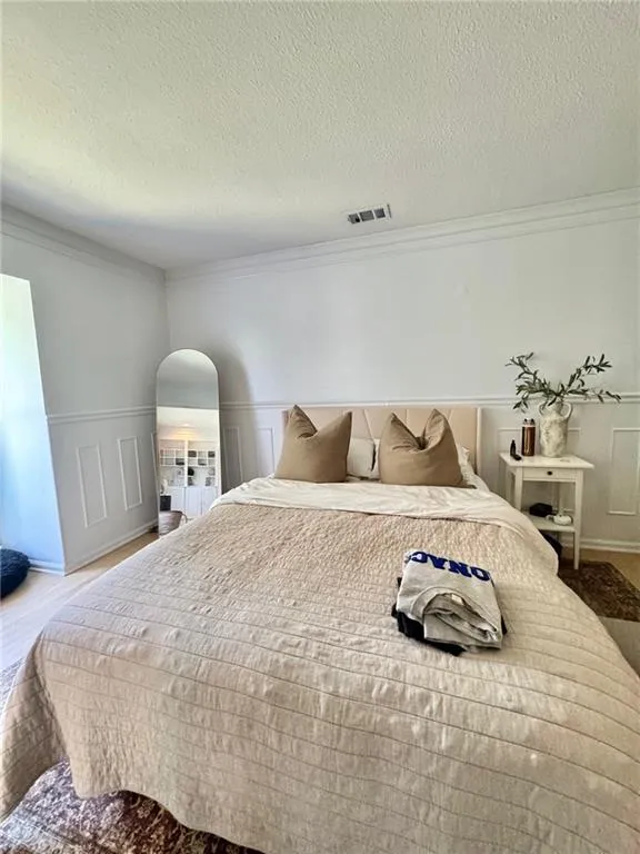 Bedroom featuring ornamental molding, a textured ceiling, a wainscoted wall, a decorative wall, and wood finished floors
