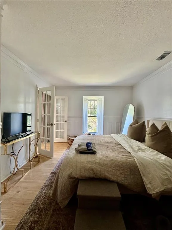 Bedroom featuring wood finished floors, a wainscoted wall, crown molding, a textured ceiling, and french doors