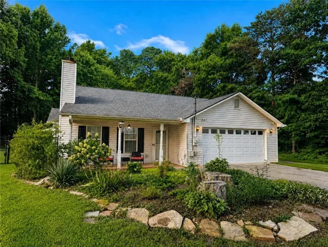 White siding exterior with a dark shingle roof, attached garage, covered front porch, and established landscaping