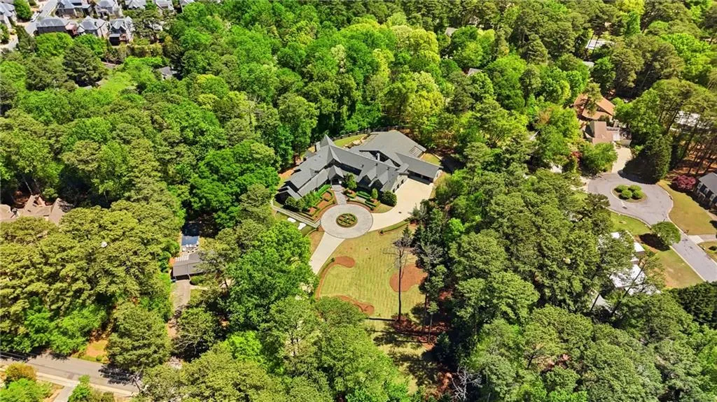 Sprawling estate featuring a multi-wing residence with dark roofing, a circular driveway, and extensive mature landscaping