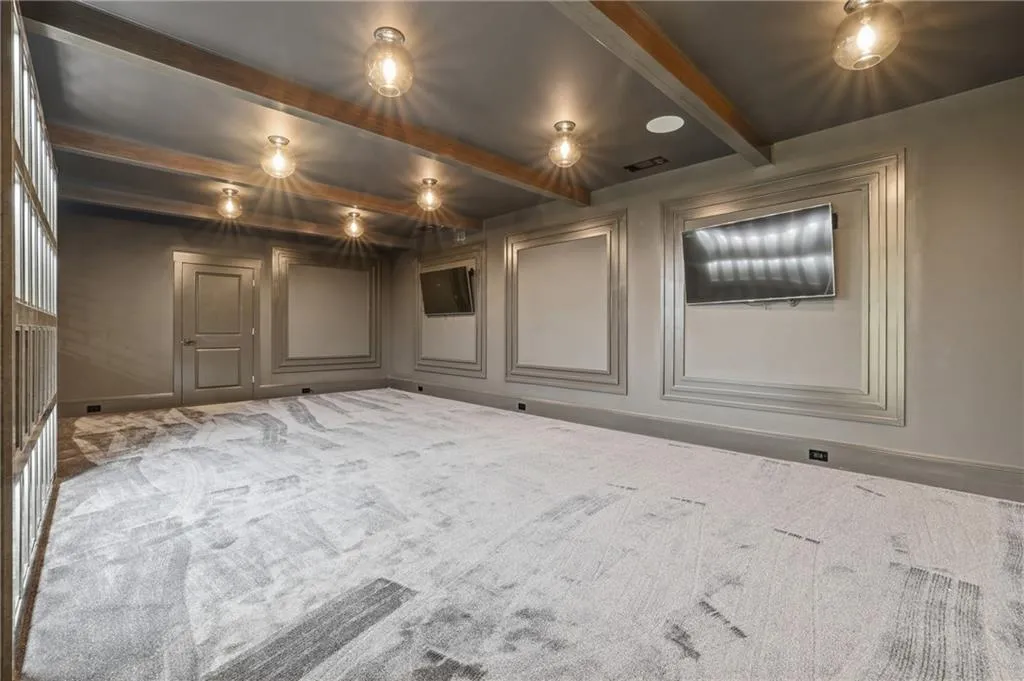 Spacious room featuring a patterned area rug, a coffered ceiling with exposed wood-finish beams, recessed lighting, and wall-mounted televisions