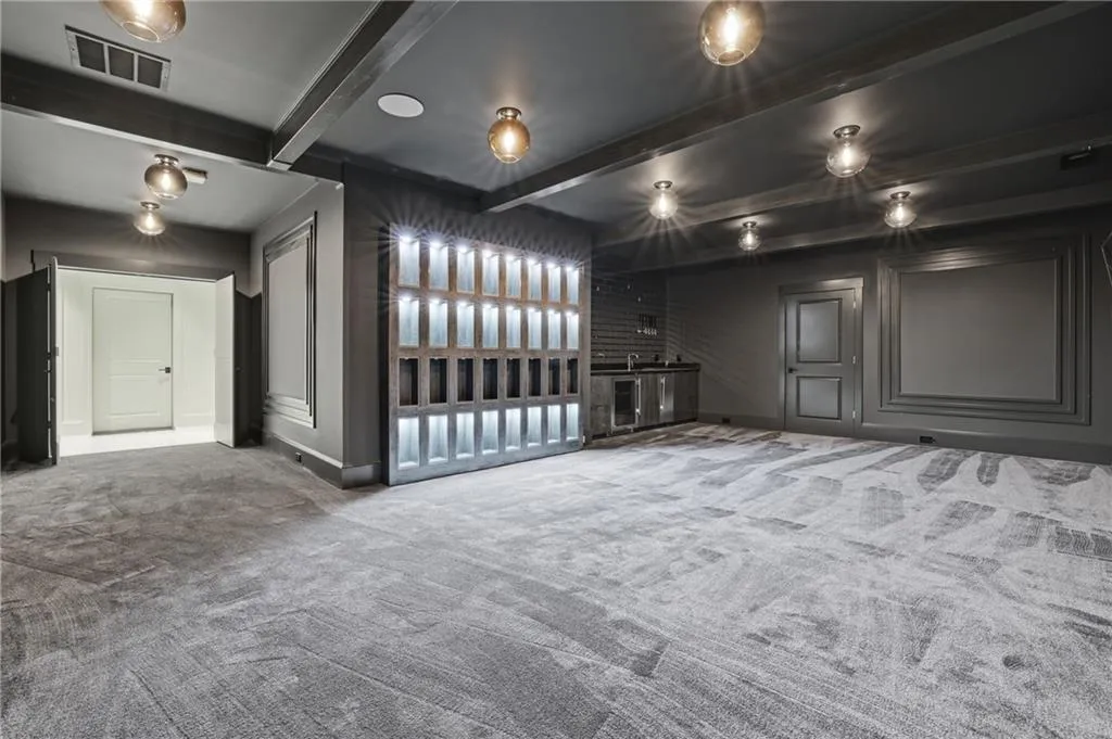 Spacious interior room featuring patterned carpet, a built-in wet bar with a sink and under-counter appliances, and a back-lit display wall
