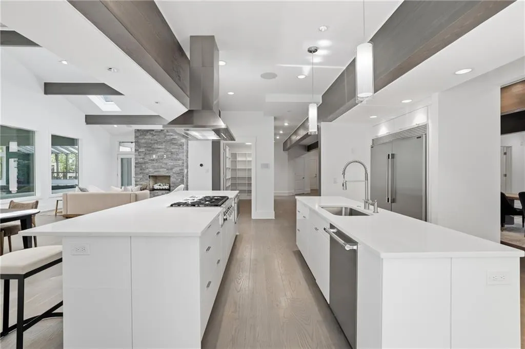 Spacious kitchen featuring two large islands with white countertops, integrated stainless steel appliances, wood-finish flooring, and exposed ceiling beams