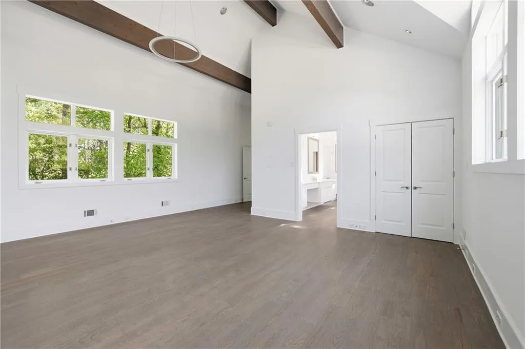Vaulted ceiling with exposed wood beams, wood-finish flooring, large multi-pane windows, double-door closet, and an attached bath with dual vanities