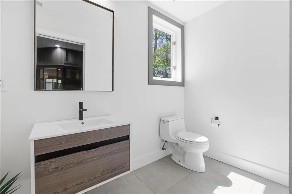 Contemporary bathroom featuring a floating wood-finish vanity with an integrated sink, a matte black faucet, a large rectangular mirror, and light gray floor tiles
