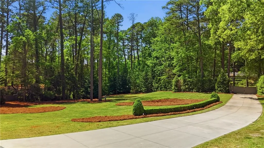 Paved driveway leading to a gated entrance, bordered by a manicured lawn with natural wood chip accents