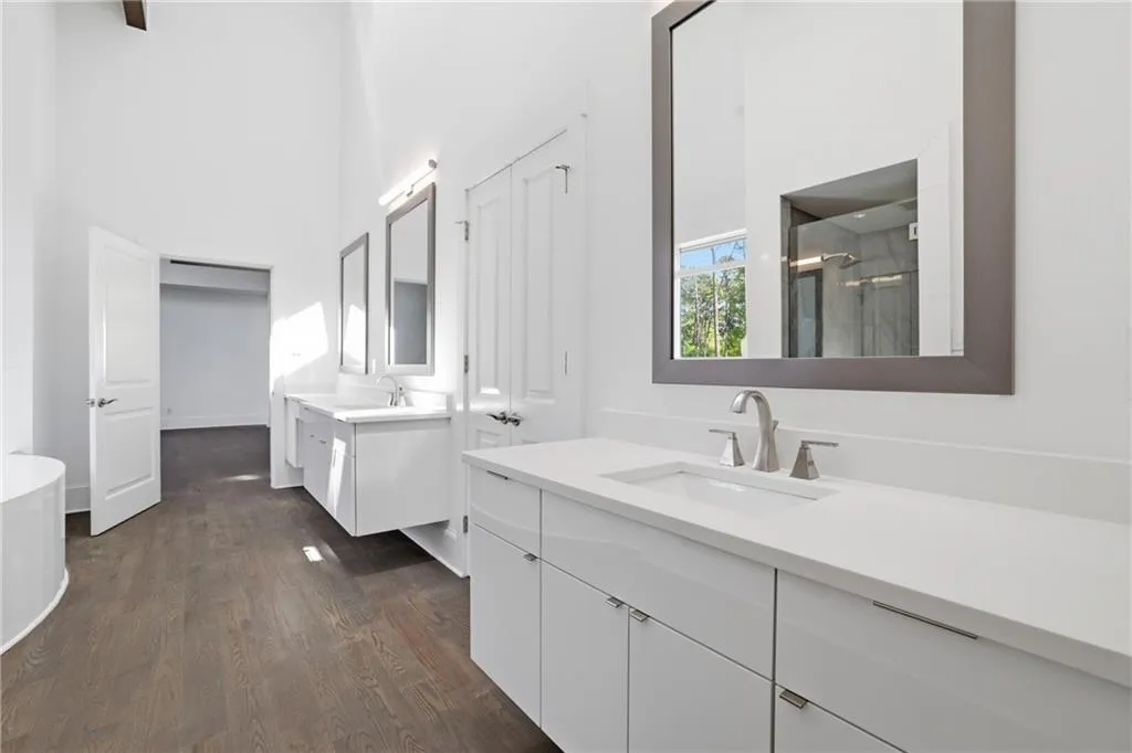 Spacious bathroom featuring a dual vanity with white cabinetry, light countertops, and wood-finish flooring
