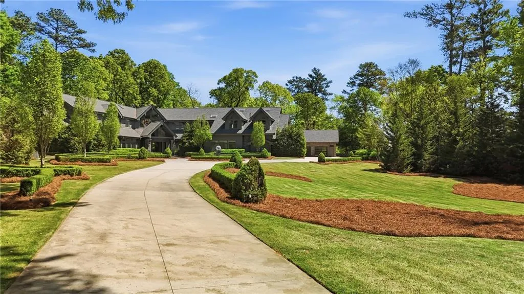 Asphalt driveway curving towards a multi-story residence with a dark facade, surrounded by manicured lawns and mature trees