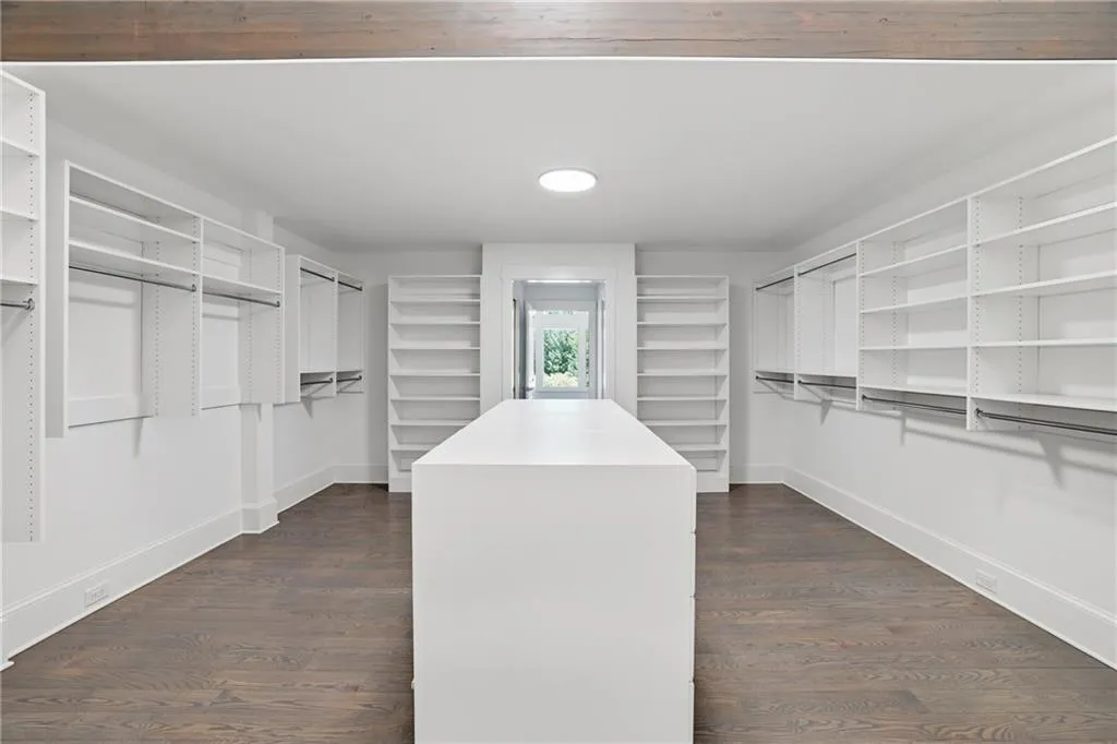 Spacious walk-in closet featuring a central island, extensive built-in shelving, hanging rods, recessed lighting, and dark wood-finish flooring