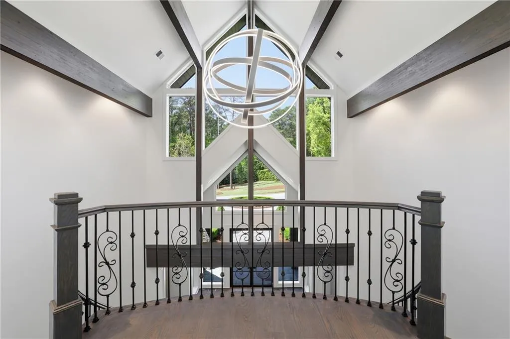 Two-story foyer featuring an ornate wrought iron railing, vaulted ceilings with exposed beams, and a contemporary spherical chandelier