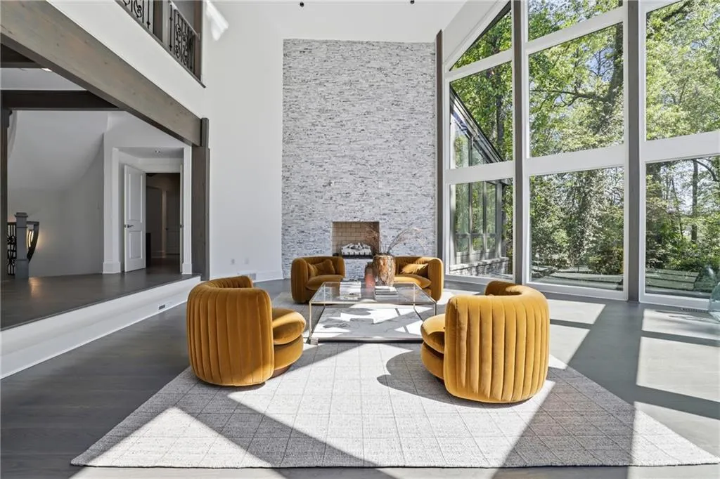 Two-story living area featuring a stacked stone fireplace, soaring ceilings, dark wood-finish flooring, and expansive floor-to-ceiling windows