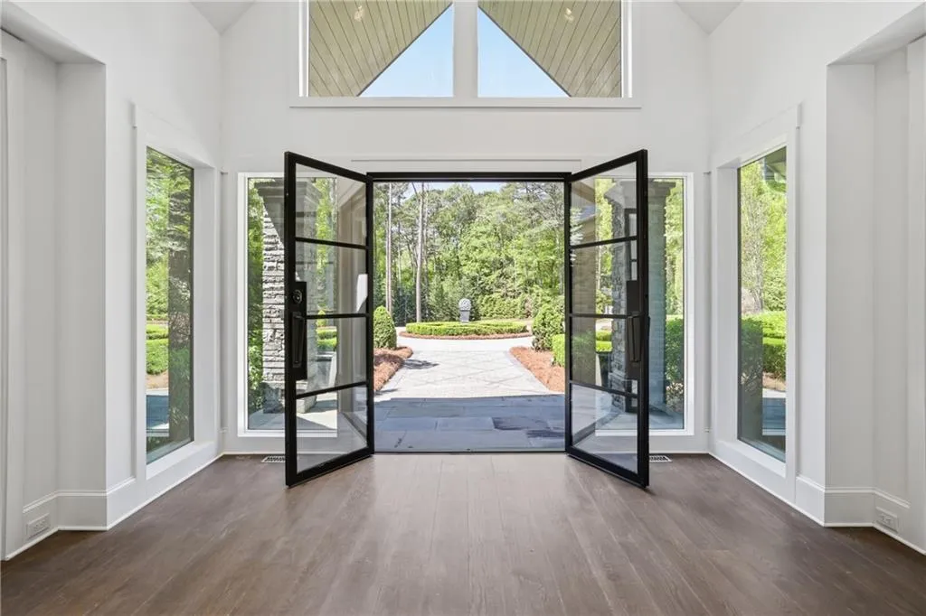 Grand entryway featuring dark-framed double glass doors, a stone paver pathway, and surrounding transom windows