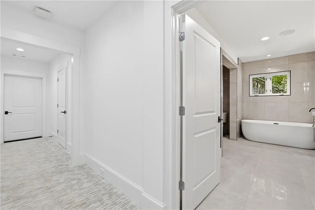 Spacious bathroom featuring a freestanding soaking tub, tiled walls, large format floor tiling, and a black-framed window