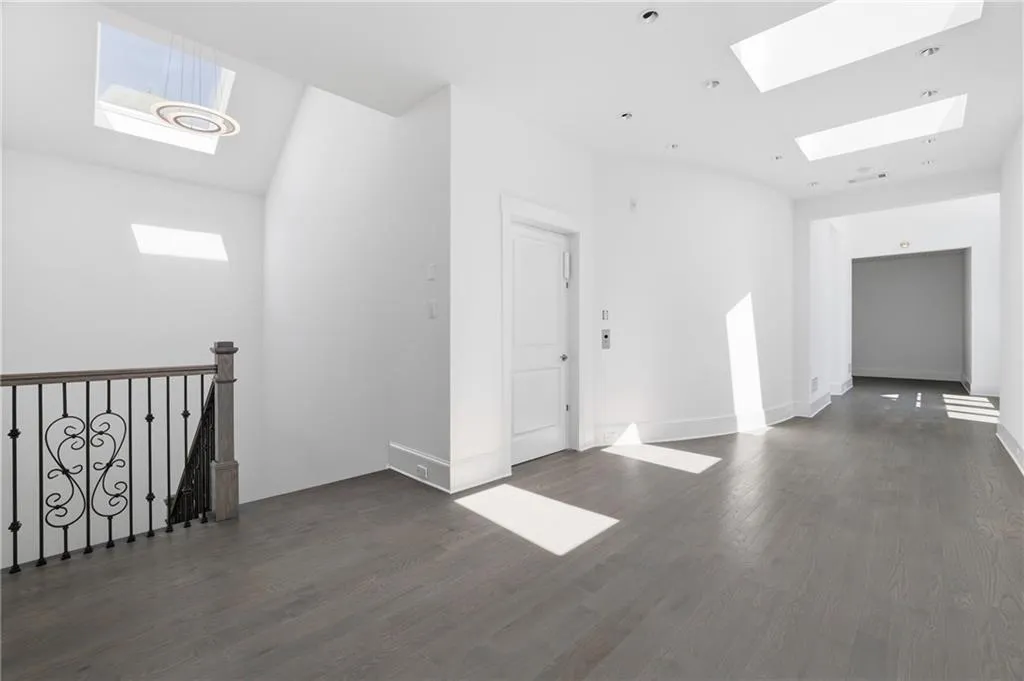 Spacious hallway with wood-finish flooring, multiple skylights, recessed lighting, and a decorative wrought iron staircase railing