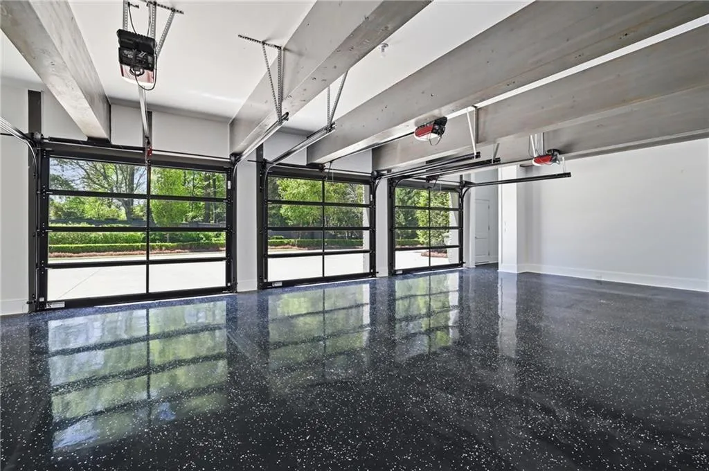 Three full-view glass garage doors with black framing, epoxy-coated flooring, and exposed ceiling beams