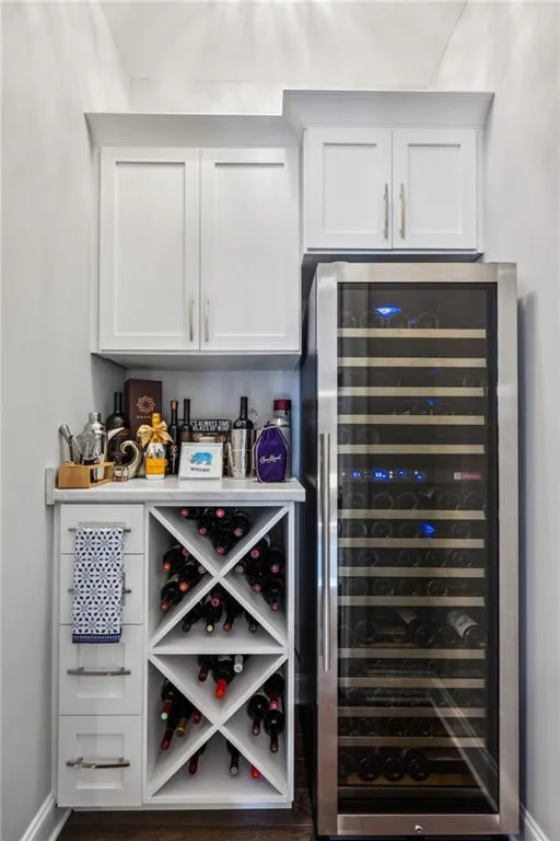 Bar featuring beverage cooler, white cabinetry, dark wood-style floors, and light countertops
