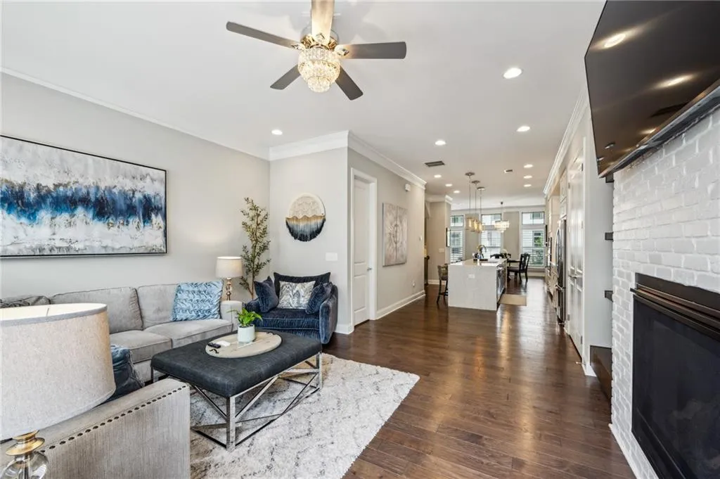 Living room with dark wood floors, a brick fireplace, recessed lighting, crown molding, and ceiling fan
