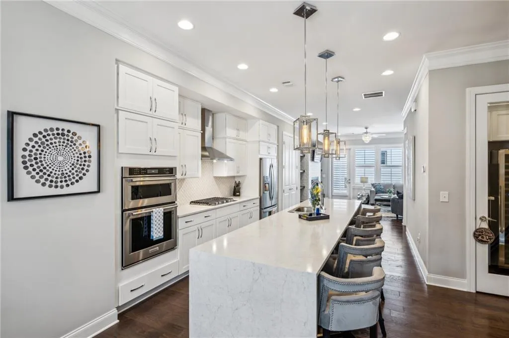 Kitchen with white cabinets, a breakfast bar, tasteful backsplash, hanging light fixtures, and dark wood flooring