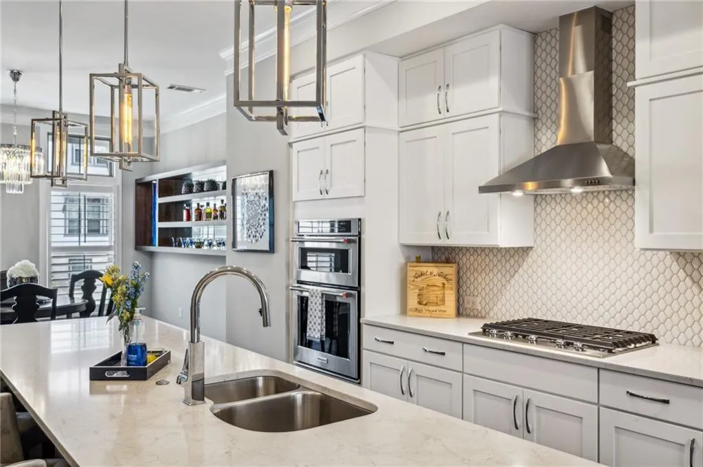 Kitchen with white cabinetry, crown molding, hanging light fixtures, wall chimney exhaust hood, and decorative backsplash