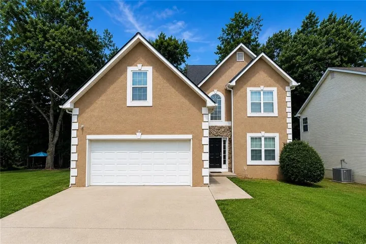 Stucco exterior with stone accents, attached two-car garage, concrete driveway, and established front landscaping
