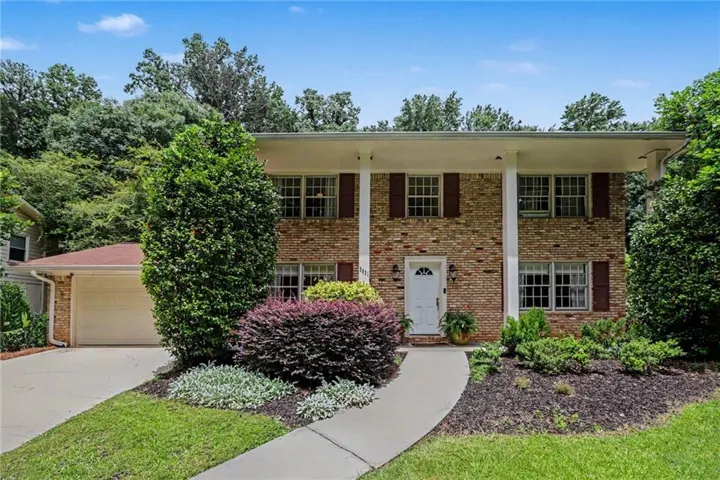 Brick residence featuring a two-car garage, white front door, shuttered windows, and a covered porch with white columns