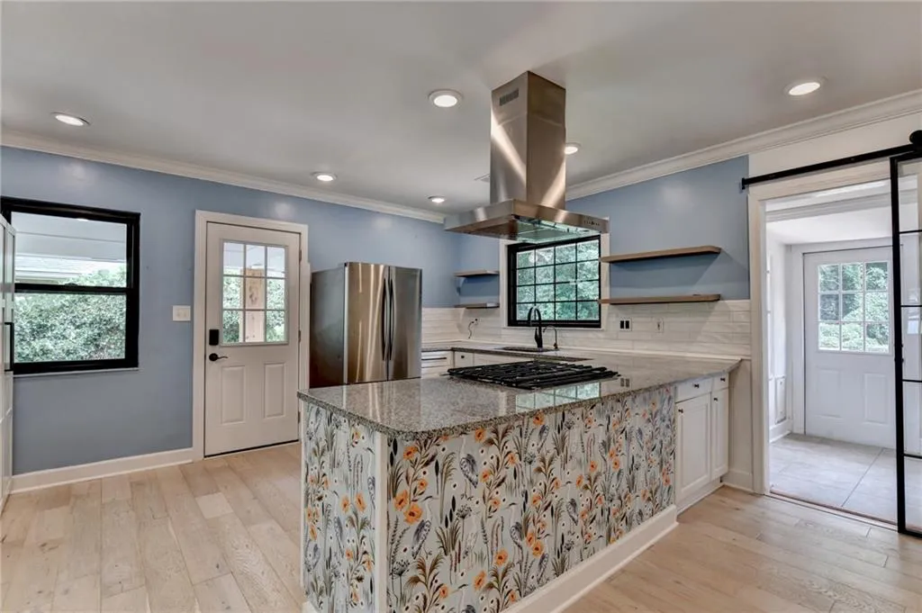 Kitchen featuring dark stone counters, decorative backsplash, island range hood, freestanding refrigerator, and crown molding