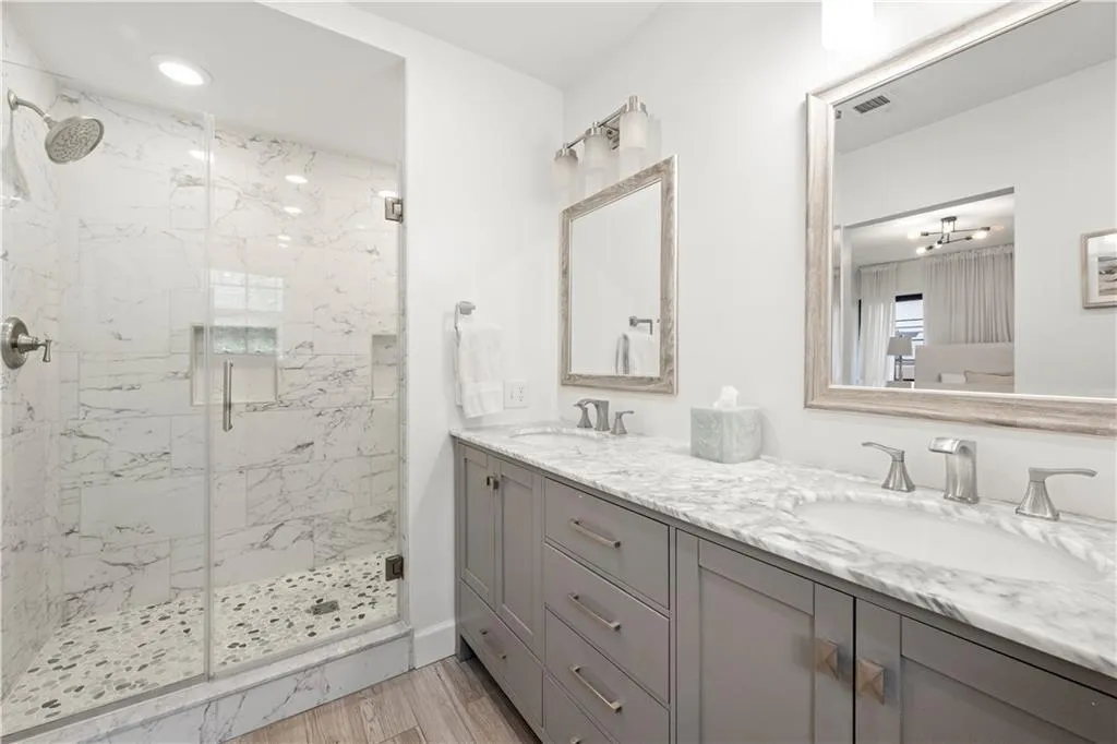 Full bath featuring a marble finish shower, double vanity, and light wood finished floors