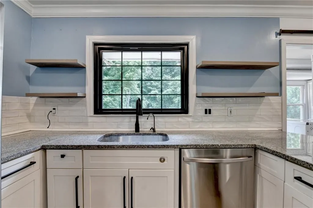 Kitchen featuring open shelves, dishwasher, dark stone counters, white cabinetry, and ornamental molding