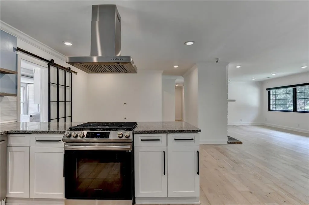 Kitchen featuring stainless steel gas range oven, dark stone countertops, island range hood, light wood-style floors, and recessed lighting