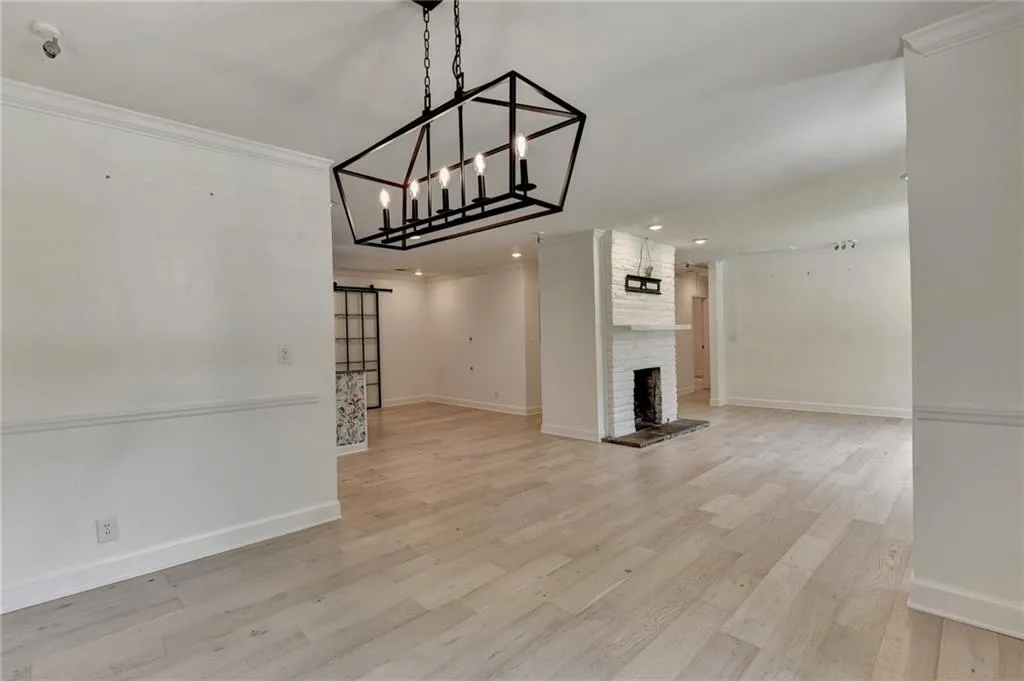 Unfurnished dining area with a barn door, light wood-style flooring, crown molding, a chandelier, and recessed lighting