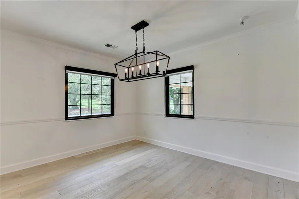 Empty room featuring healthy amount of natural light, ornamental molding, light wood-style floors, and a chandelier