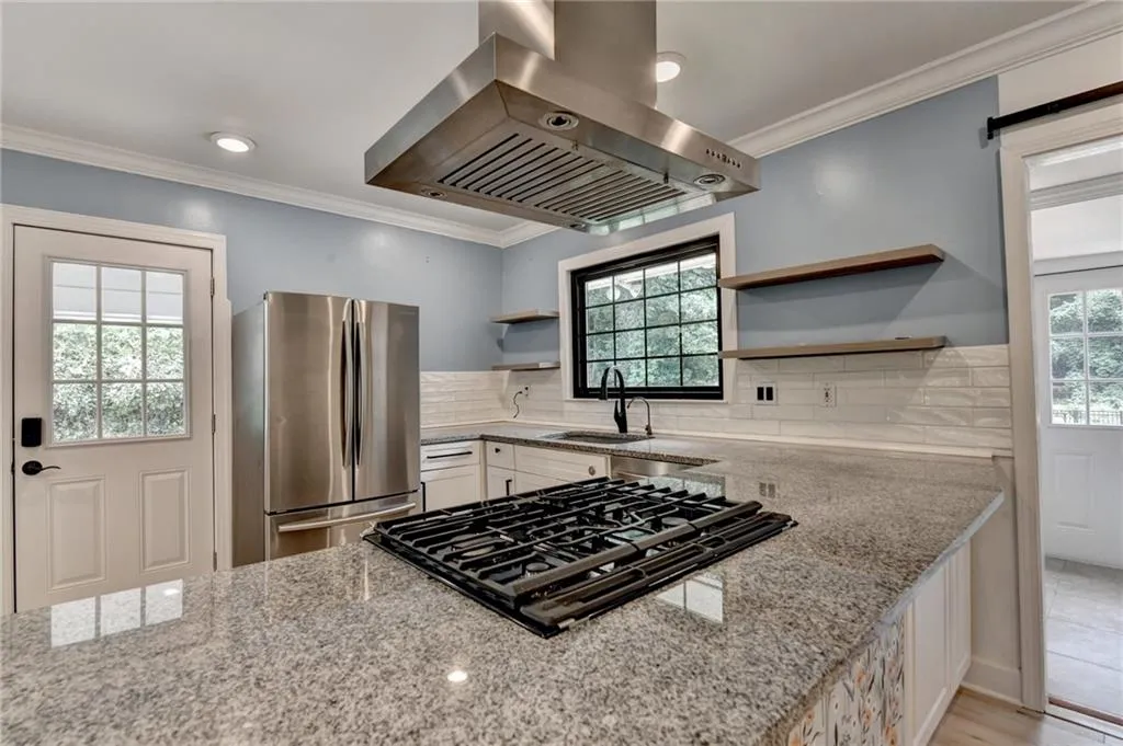 Kitchen featuring island range hood, freestanding refrigerator, ornamental molding, plenty of natural light, and light stone counters